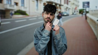 Kot ceketli genç adam, arka planı bulanık, şehir yaşam tarzını ve modern kimlik kavramlarını gösteren bir kart tutuyor..