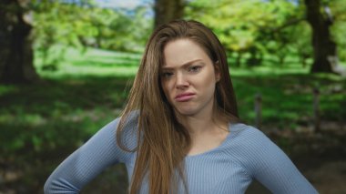 Güneşli bir parkta, yeşil ağaçların ve çimenlerin ortasında, yüzü buruşmuş ellerle kaşlarını çatan kadın iğreniyor..