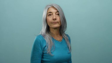 Mavi arka planda beyaz saçlı bir kadın zarif bir şekilde yaşlandığını gösteren sakin bir varlık yayıyor ve basitlik ve zarafetle gücünü gösteriyor..