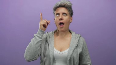Kadın parmağını yukarı kaldırır ve gözleri stüdyoda mor arka planda ayrık dudaklarla kapatır; kendine güven.