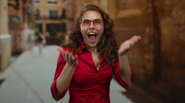 Kırmızı gözlüklü ve kırmızı gömlekli bir kadın sıcak, güneşli bir ortamda güvenle gülümsüyor..