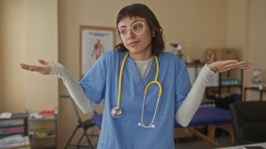 Klinikteki mavi önlüklerin üzerinde sarı steteskoplu el ve çıplak kollarını silken bir kadın..