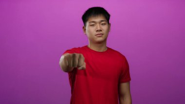Kırmızı tişörtlü genç Çinli adam güvenlik ve güç iletmek için izole edilmiş pembe arka plana doğru yumruğunu uzattı..