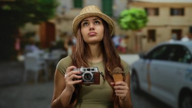 Kalabalık bir sokakta elinde kamera ve dondurma tutan kadın güneşli gökyüzünün altında hasır şapka takarak seyahat etmekten zevk alıyor. Gezgin şehveti ve İspanyol kültürünün özünü ifade ediyor..