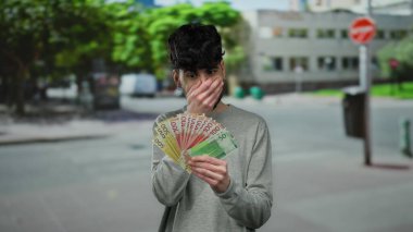 Genç adam, sokak hayatı ve para heyecanı sergilenen şehir ortamında Norveç kronunu elinde tutuyor..