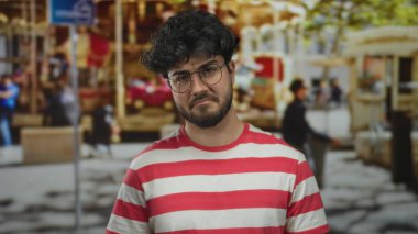 Sokak ortamında gözlüklü ve sakallı, kırmızı beyaz çizgili gömlek giyen üzgün, şehir geçmişi bulanık genç bir İspanyol..