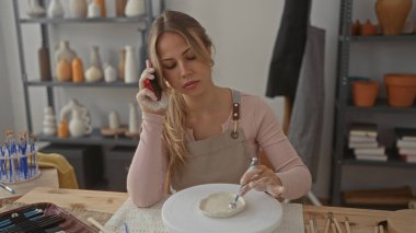 Önlüklü kadın stüdyoda kil ve tekerleği nazikçe şekillendirmek için elleri kullanır; yaratıcılık farkındalığı odak noktası.