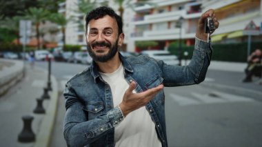 Sakallı İspanyol bir adam canlı bir sokak sahnesinde arabanın anahtarlarını tutuyor, şehir yaşamını ve modern ulaşımı gözler önüne seriyor..