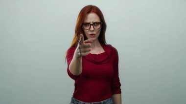 Öfkeyle işaret eden ve işaret veren bir kadın kırmızı saçlı, gözlüklü ve beyaz arka planda izole edilmiş kırmızı bluzu olan buraya gelir..