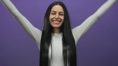 Genç İspanyol kadın, elleri mor arka planda bir kalp şekli oluşturur, izole edilmiş bir ortamda neşeyle gülümser..