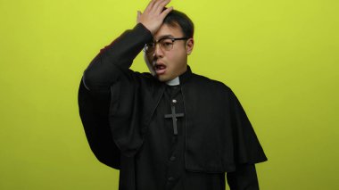 Gözlüklü ve çapraz hareketli Asyalı bir adam, parlak sarı bir arkaplan karşısında duygusal ya da ruhani bir anı işaret ediyor..