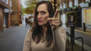 Kalabalık bir şehir caddesinde kararlı bir kadın, şehir atmosferini kendine güvenen bir ifadeyle ve arka planda bulanık bir şekilde açık havada günlük kıyafetlerle yakalıyor..