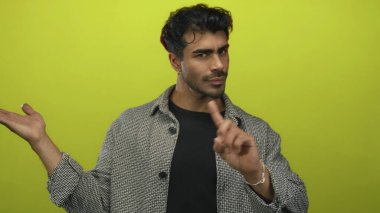 Sarı ceketli İspanyol genç adam, sarı stüdyoda avuç içini ve parmağını açık tutuyor; belirsizlik..