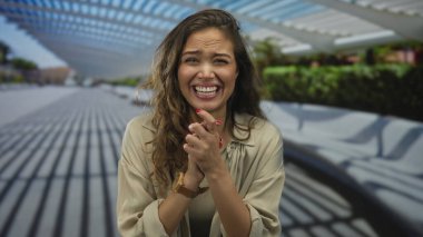 Güneşli bir şehir ortamında neşeli bir şekilde gülümseyen kadın modern mimariyle yürüme yolunda gölgeler bırakıyor, parlak bir günde mutluluğu ve hayat dolu enerjiyi sergiliyor..