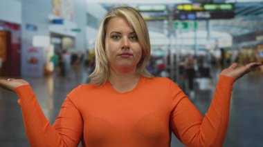 Turuncu kazaklı genç sarışın kadın, kalkış kapılarının yanındaki tezgahta yoğun havaalanı terminalinde el sıkışıyor; kararsızlık.