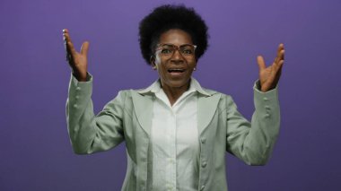 Gözlüklü ve afro saçlı Afrikalı kadın, mor bir arka plan karşısında gözlerini şakayla kapatıyor..