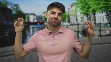 Pembe polo tişörtlü genç İspanyol adam, ellerinde alaycı bir sırıtışla sokakta el kol hareketi yapıyor..