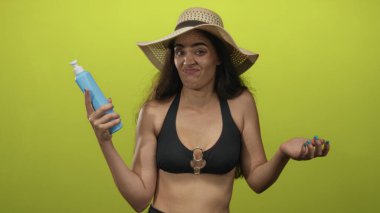 Hasır şapkalı kadın elinde mavi losyon şişesi tutuyor ve stüdyoda şişeyi işaret ediyor; şüphecilik.