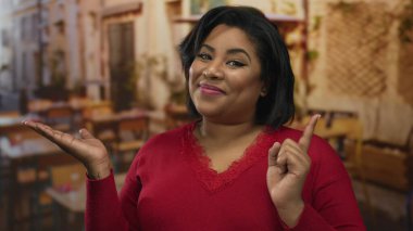 Dışarıdaki terasta gülümseyen ve kamerayı işaret eden bir kadın, kırmızı kazak giyiyor, canlı, sıcak atmosferli şehir yemeği sahnesi sergiliyor..