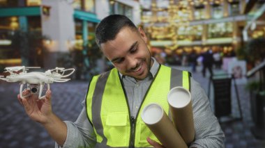 Adam gülümsüyor ve bir dron tutuyor ve modern binanın içindeki cihazı incelerken planları yuvarlıyor; yenilik.