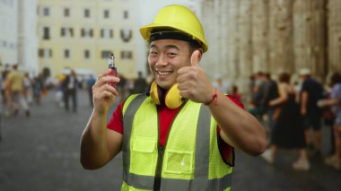 Miğfer ve çelik yelek giyen adam işlek şehirde gülerken elektronik sigara tutuyor..