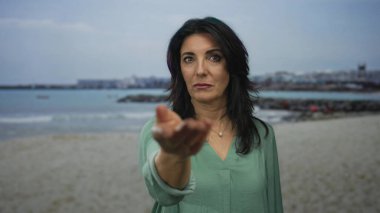 Uzak okyanus dalgaları ve görünür rıhtımı olan kumlu sahile parmağını gösteren bir kadın..