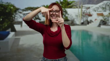 Oteldeki havuzun yanında gülümseyen bir kadın elleriyle yüzünü çerçeveliyor ve rahat bir atmosfer yaratıyor..