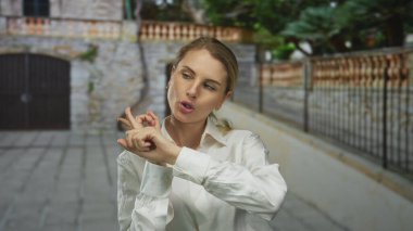 Çekici bir Avrupa avlusunda neşeli bir şekilde dışarıyı gösteren kadın beyaz gömlekli genç bir sarışını resmediyor. Taş bir duvara ve demir kapıya dayanıyor..