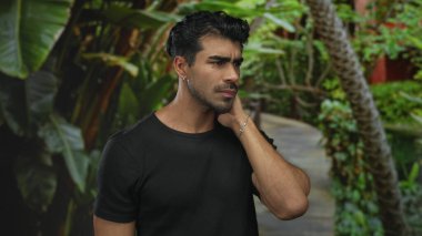 Genç Hispanik adam orman yolunda boyun ağrısı içinde, servikal bölgesini gergin bir duruşta tutuyor;.