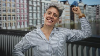 Çizgili tişörtlü gülümseyen beyaz kadın kanal kollarını esnetiyor; güç ve gurur motivasyonu..