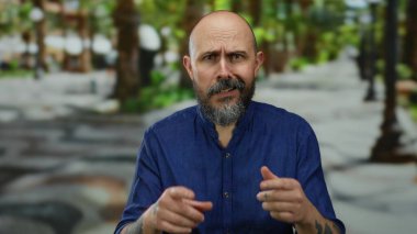 Bulanık bir şehir caddesinde arka planda ağaçlarla dışarıda duran sakallı adam.