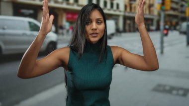 İnsanlar ve araçlar arka planda hareket ederken İspanyol genç kadın kentin işlek caddesinde güvenli bir şekilde dikiliyor ve canlı şehir atmosferini yakalıyor..