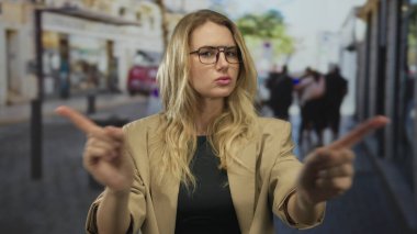 Kadın, şehir merkezinde gözlük ve bej ceket giyerken, açık havada şehir ortamını onaylamadığını belirtirken, hareketli şehir caddesinde parmaklarıyla hareket etmez..
