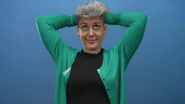 Stüdyoda kısa saçlı, yeşil hırka giyen, elleri başının arkasında olan bir kadın..