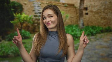 Taş duvar ve yeşillik zemin ile eski kasabanın kaldırım taşı caddesinde kolsuz üst işaret parmağı olan bir kadın..