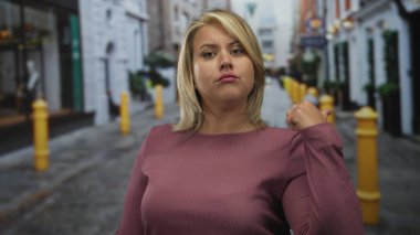 Sarışın genç bir kadın şehir merkezinde kaldırım taşı caddesinde başparmağıyla işaret ediyor..