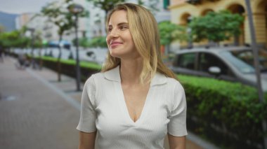 Çevresi yemyeşil ve şehir mimarisi ile çevrili canlı bir şehir caddesinde güven içinde yürürken gülümseyen bir kadın özgürlük ve macera duygusunu resmediyor..