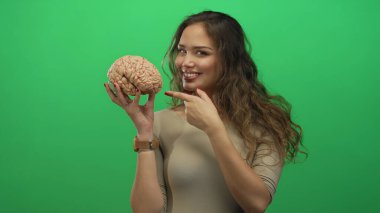 Beyin modelini yeşil arka planda tutan kadın kendine güvenen bir ifadeyle zeka odaklanma ve bilgi gösteriyor.