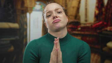 Kapalı halı dükkanında yeşil balıkçı yaka kazak giyen genç beyaz kadın özür diliyor..