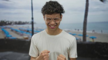 Erkek yumruğunu sıkar ve kollarını kaldırıp bağırır gözlük takar ve güneşli sahil sahilinde beyaz bir tişört giyer; heyecan zaferi.