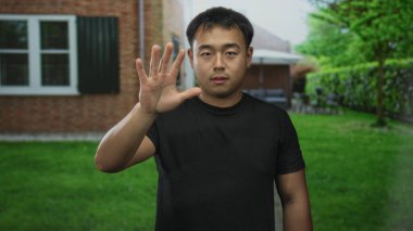 Siyah tişörtlü adam yeşil çimenlikteki banliyö evinin girişini işaret ediyor; kararlılık.