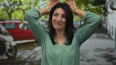 İspanyol orta yaşlı kadın gülümser ve tavşan kulaklı el kaldırır şehir caddesinde jest, neşeli eğlence kaprisli.