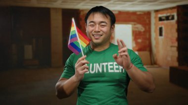 Bitmemiş inşaat sahasında gökkuşağı bayrağı tutan genç adam, LGBT desteği ve Asyalı temsilciliği simgeliyor..