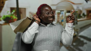 Sokakta gülümseyen bir kadın elinde alışveriş torbalarıyla dışarıda neşe içinde bekliyor..