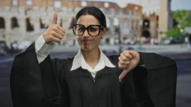 Genç İspanyol kadın yargıç, Roma kolezyumu geçmişi olan, modern hukuk ve antik Roma şehir atmosferini harmanlayan, yasal üniformayla yukarı ve aşağı baş parmak gösteriyor..