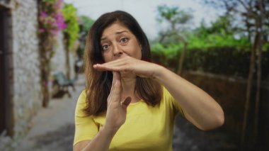 Kadın, şehir caddesinde ellerinin begonville ve taş duvarla kaplı olduğu bir yerde gün ışığında jest yapıyor; tefekküre ara verin..