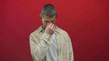 İzole edilmiş kırmızı arka planda yüzü olan bir adam stresli ya da endişeli, gözleri kapalı sıradan bir gömlek giyiyor..
