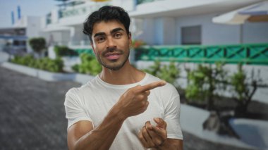Genç İspanyol adam elleri açık hareket eder ve bina girişinin önünde çıplak kollarını gösterir; iletişim.