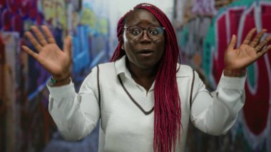 Şehirli duvar yazısı arka planına karşı anlamlı gözlerle kendini gösteren bir kadın, canlı bir sokak aralığında bireyselliği ve duyguyu ön plana çıkarıyor..