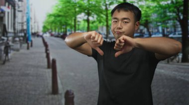 Siyah tişörtlü adam, yeşil ağaçlar ve bisikletlerle kaplı sokakta baş parmaklarını aşağı gösteriyor..